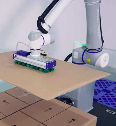 Cobot mit Vakuumgreifer hebt eine Platte über gestapelte Kartons